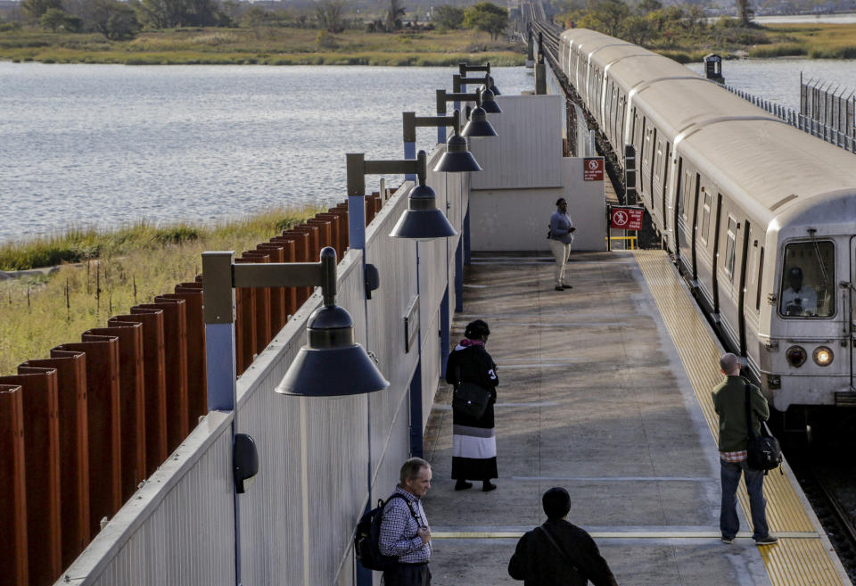 FILE - A subway train slows as it makes its way into the Broad Channel station next to a seawall installed after Superstorm Sandy washed out sections of the tracks in October 2012, in the Rockaways section of Queens, New York, on Oct. 21, 2014. As weather becomes more extreme and unpredictable caused by climate change, transit officials say that more needs to be done to prepare the East Coast's vital transit systems. (AP Photo/Mark Lennihan, File)