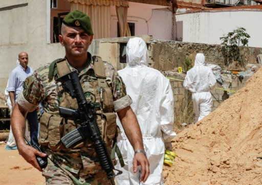 A Lebanese army soldier walks past military intelligence forensic investigators ar the scene where two drones came down in the vicinity of a media centre of the Shiite Hezbollah movement