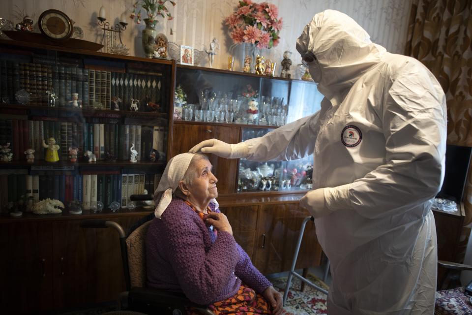 In this photo taken on Tuesday, May 26, 2020, Father Vasily Gelevan, wearing a biohazard suit and gloves to protect against the coronavirus, blesses Tamara Trusova, 90, who is suspected of having coronavirus, at her apartment in Moscow, Russia. In addition to his regular duties as a Russian Orthodox priest, Father Vasily visits people infected with COVID-19 at their homes and hospitals. (AP Photo/Alexander Zemlianichenko)