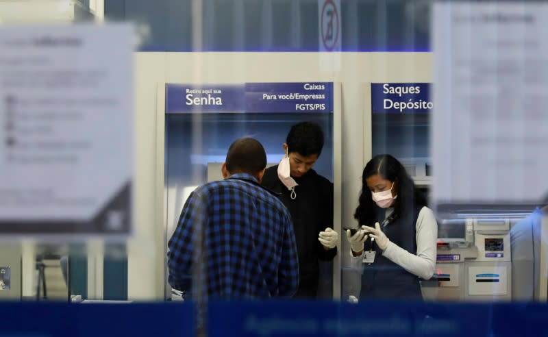 Employees wear protective masks and gloves inside a bank agency as they talk with a client during the coronavirus disease (COVID-19) outbreak in Porto Alegre