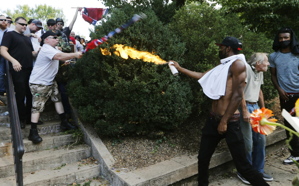 FILE - In this Aug. 12, 2017, file photo, a counterdemonstrator uses a lighted spray can against a white nationalist demonstrator at the entrance to Lee Park in Charlottesville, Va. (AP Photo/Steve Helber, File)