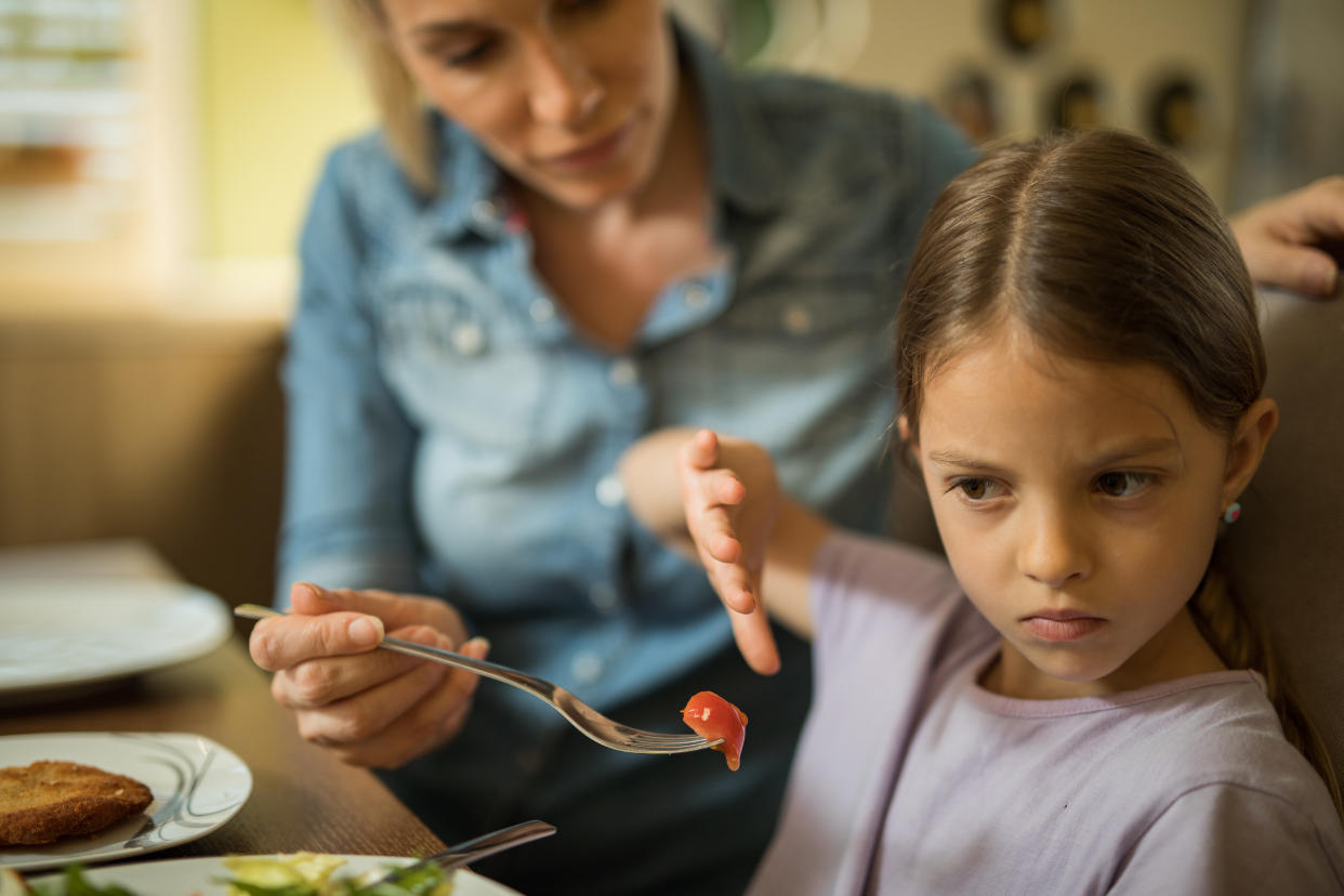 Displeased girl refusing to eat cherry tomato while her mother is feeding her.