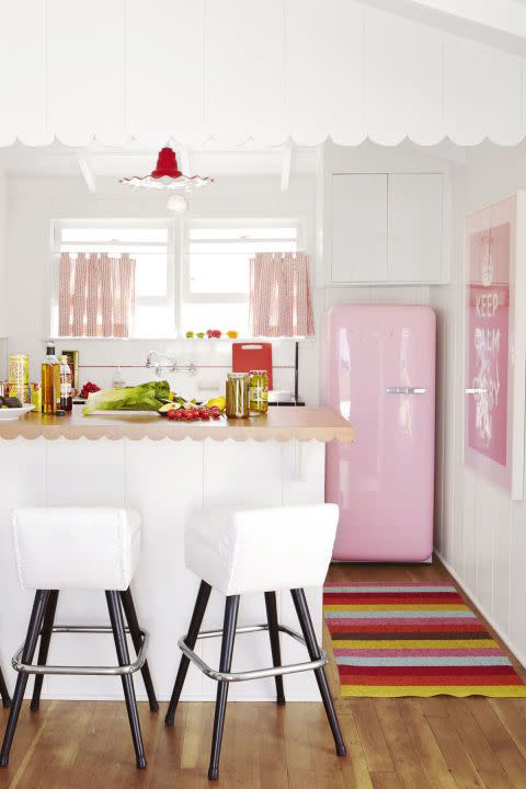white kitchen with pink accents, including the retro style fridge, and pops of red in the light fixture and multicolored striped rug