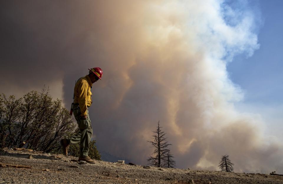 A firefighter walks along a bare ridge as smoke rises behind