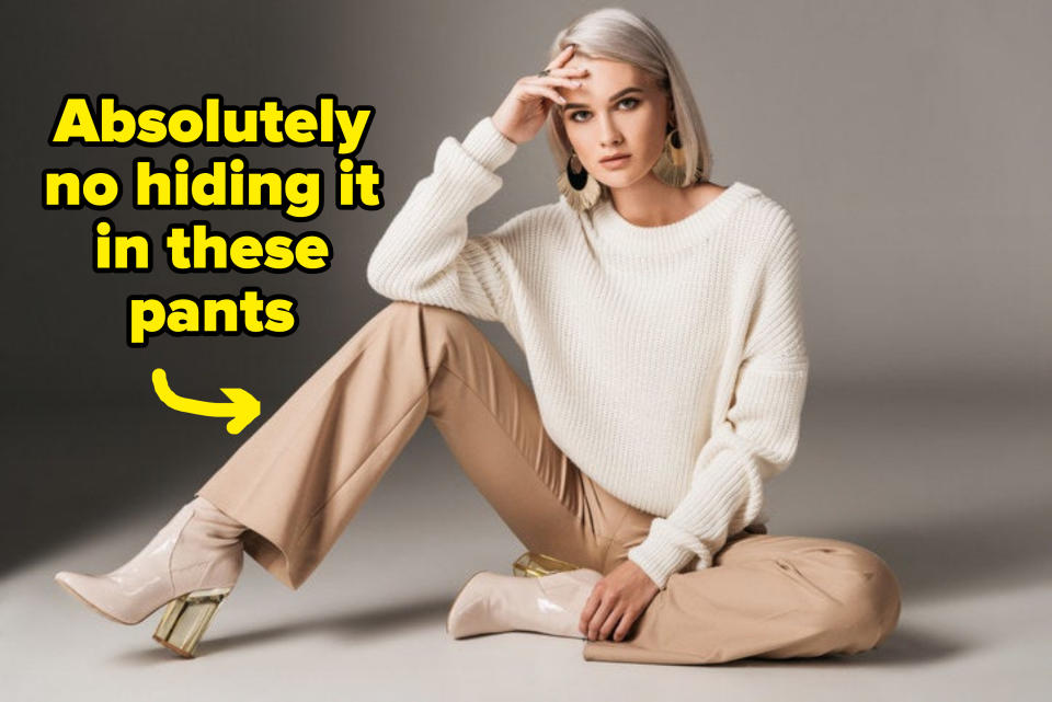 fashionable woman posing in white trendy sweater, beige pants, and autumn heels, on gray, with the text "absolutely no hiding it in these pants"