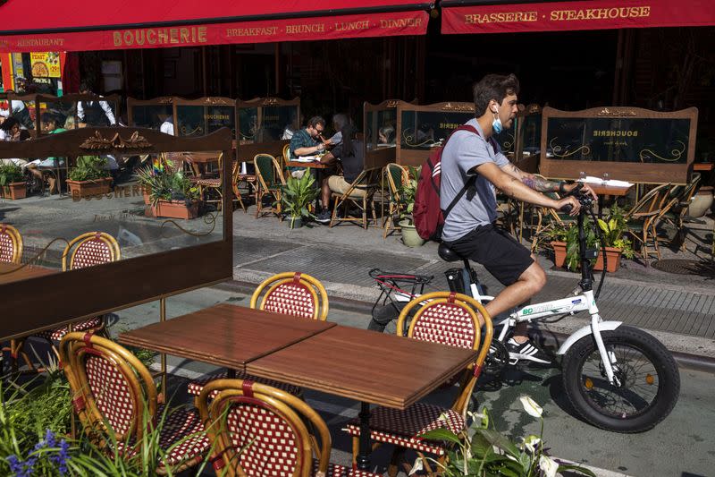 A man on a bike rides past customers social distancing in outdoor seating at a restaurant in New York City