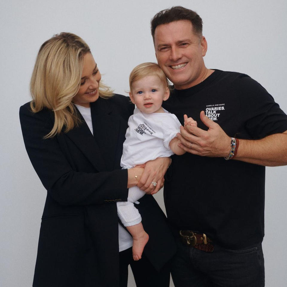 Karl Stefanovic pictured in a black t shirt, holding his daughter with his partner.