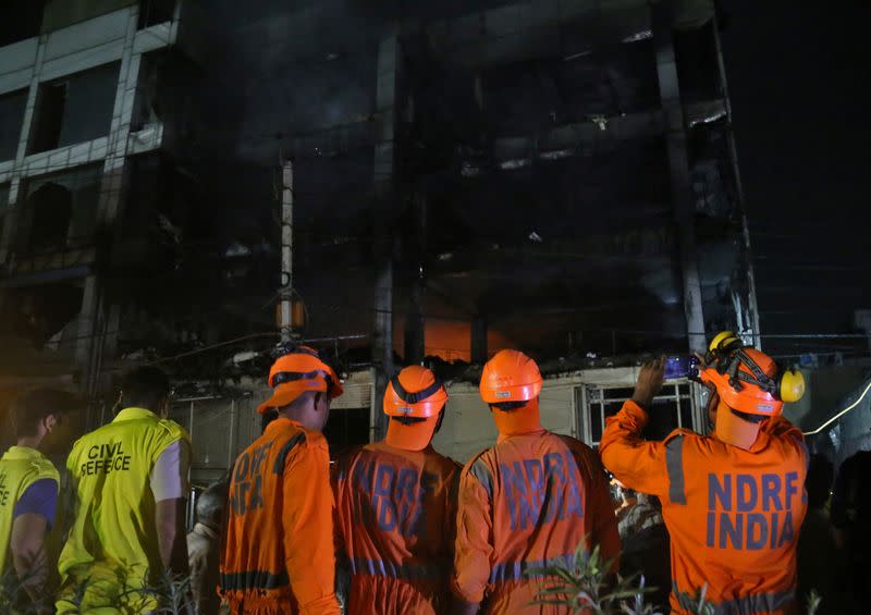 Members of NDRF stand as fire fighters try to douse a fire that broke out at a commercial building in Delhi's western suburb