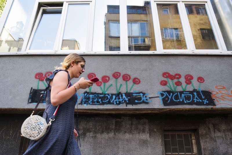 A woman walks next to a graffiti with the words reading "Ukraine is Russia", in Belgrade
