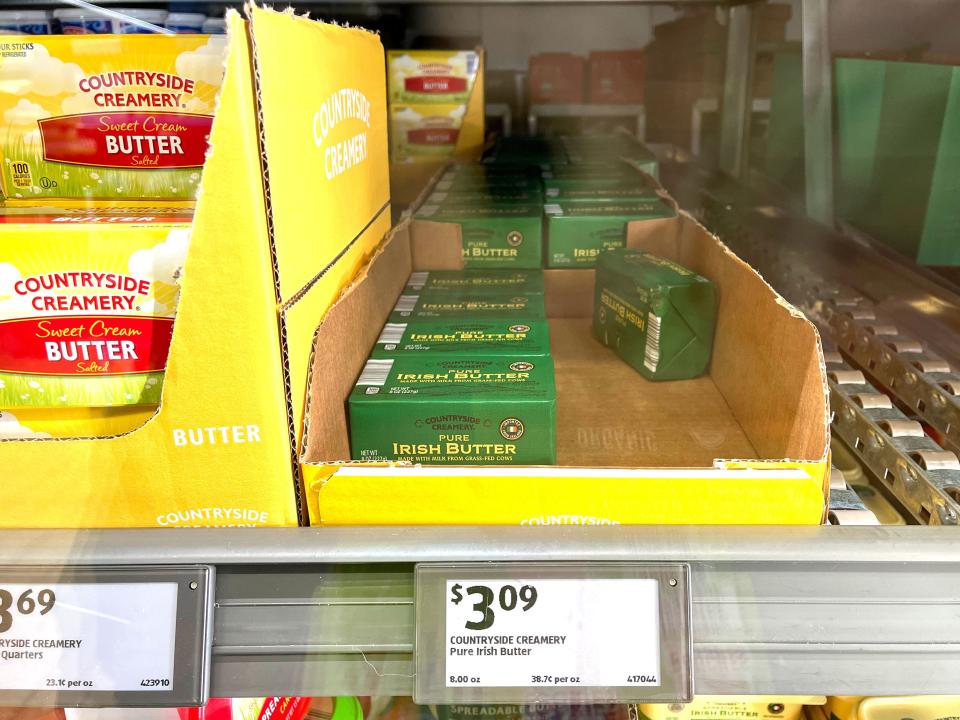 Boxes of Countryside Creamery pure Irish Butter in an open cardboard box in the refrigerator at Aldi. The price tag underneath reads $3.09.