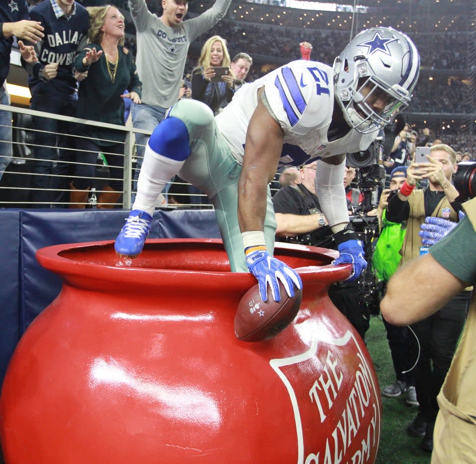 Dallas Cowboys running back Ezekiel Elliott climbs into a Salvation Army kettle
