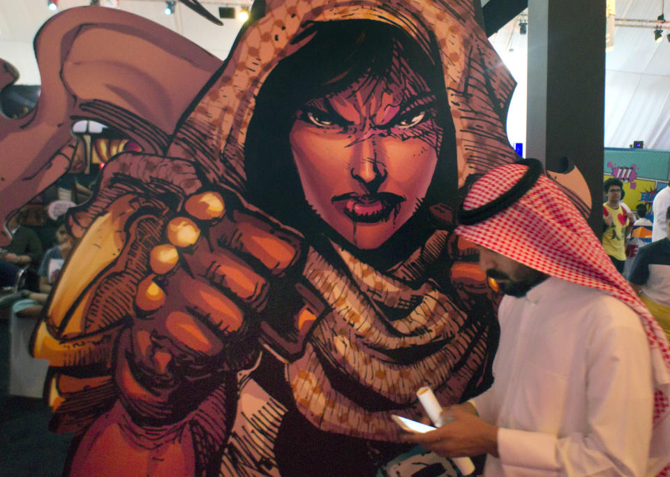 FILE - In this Friday, Feb. 17, 2017, file photo, a visitor walks past a banner showing Latifa, Saudi super woman character, during the Saudi Comic Con (SCC) which is the first event of its kind to be held in Jiddah, Saudi Arabia. The kingdom, which bans movie theaters and other entertainment venues, is challenging its ultraconservative image and loosening the reins on fun by opening its doors to live shows, including some American ones. (AP Photo, File)