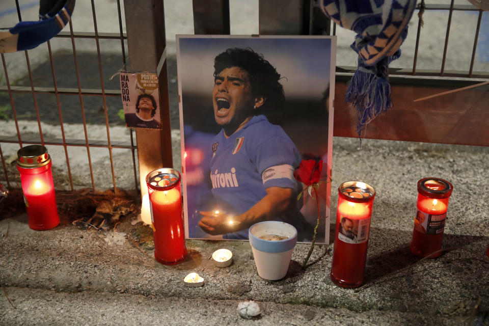 Candles are placed next to a picture of soccer legend Diego Maradona outside the San Paolo Stadium in Naples, Italy, Wednesday, Nov. 25, 2020. Diego Maradona has died. The Argentine soccer great was among the best players ever and who led his country to the 1986 World Cup title before later struggling with cocaine use and obesity. He was 60. (AP Photo/Alessandra Tarantino)