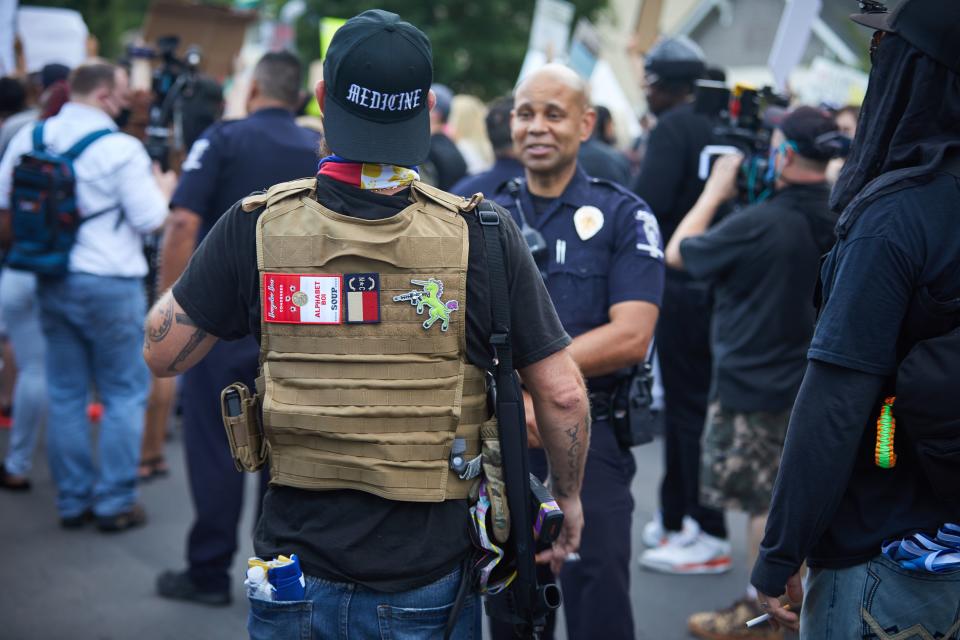 A member of the far-right militia, Boogaloo Bois, walks next to protestors demonstrating outside Charlotte Mecklenburg Police Department Metro Division 2 just outside of downtown Charlotte, North Carolina, on May 29, 2020. - The protest was sparked by protests in Minneapolis, over the death of George Floyd, a black man who died after a white policeman kneeled on his neck for several minutes. In Charlotte, CMPD Metro Division 2 was home to CMPD officer, Wende Kerl, who shot and killed Danquirs Franklin outside of a Burger King on March 25, 2019. CMPD found that officer Kerl operated in the constraints of the law but later a citizen review board would find that the officers actions were not justified. No charges were ever brought. (Photo by Logan Cyrus / AFP) (Photo by LOGAN CYRUS/AFP via Getty Images)