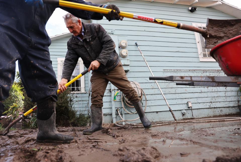 SAN DIEGO, CALIFORNIA - JANUARY 23: Family members clean mud from a home damaged by flooding, with the floodwater line visible on the house, the day after an explosive rainstorm deluged areas of San Diego County on January 23, 2024 in San Diego, California. The intense rains forced dozens of rescues while flooding roadways and homes and knocking out electricity for thousands of residents.