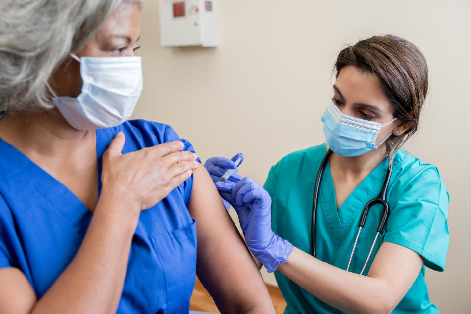 A health-care practitioner gives a vaccine to an older adult patient. Both people are wearing face masks to prevent transmission of viruses like COVID, flu and RSV. (Getty Images)