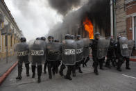 La policía antimotines forma un cordón mientras salen llamas de la sede del Congreso después de que manifestantes incendiaran una parte del edificio, el sábado 21 de noviembre de 2020, en Ciudad de Guatemala. Cientos de manifestantes irrumpieron en el Congreso de Guatemala y quemaron parte del edificio el sábado en medio de las crecientes manifestaciones contra el presidente Alejandro Giammattei y el Poder Legislativo por la aprobación de un presupuesto general para el año próximo que recortó el gasto en educación, salud y lucha por los derechos humanos. (AP Foto/Oliver De Ros)