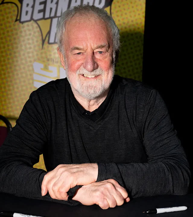 Bernard Hill smiles for a photo behind a table wearing a black shirt