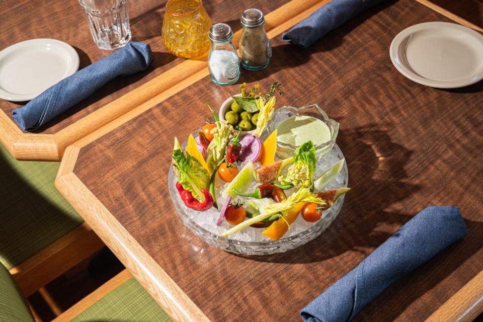 A bowl of vegetables, olives and a green dip on ice.