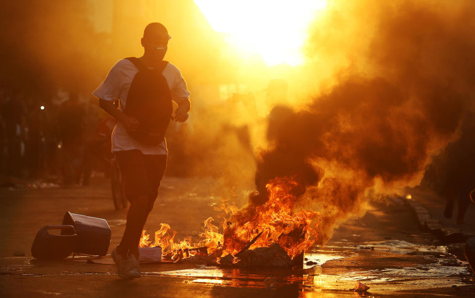 A demonstrator runs near a burning garbage pile during confrontations with police, in protest against the increase of bus fares, outside the central train station, in Rio de Janeiro, Brazil, Thursday, Feb. 6, 2014. Last year, millions of people took to the streets across Brazil complaining of higher bus fares, poor public services and corruption while the country spent billions on the World Cup, which is scheduled to start in June. (AP Photo/Leo Correa)