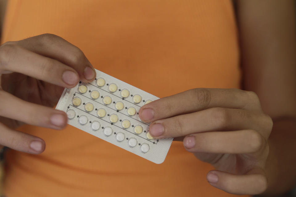Person holding a birth control pill pack in front of their orange shirt