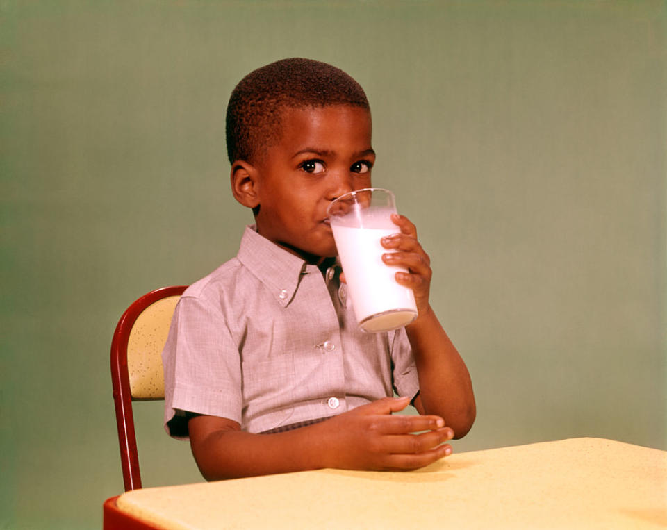 Young boy sitting at a table, drinking a glass of milk, and looking at the camera