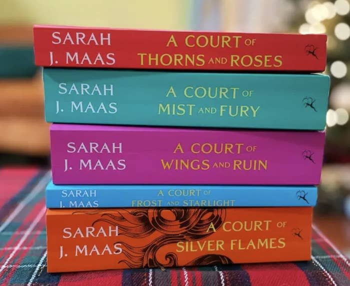 A stack of books by Sarah J. Maas is shown, including titles "A Court of Thorns and Roses," "A Court of Mist and Fury," "A Court of Wings and Ruin," and "A Court of Silver Flames."