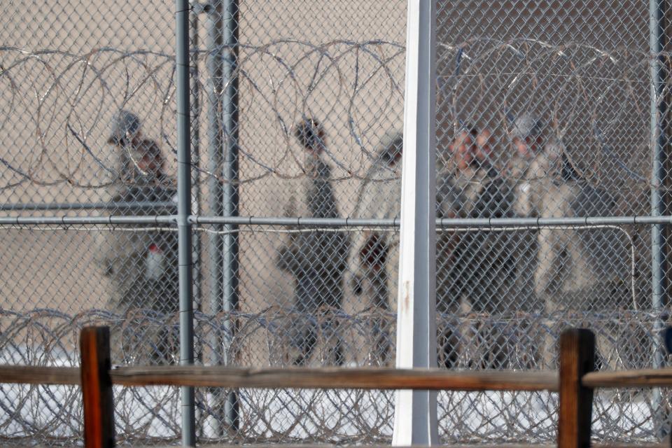 Federal inmates are seen through barbed fencing.