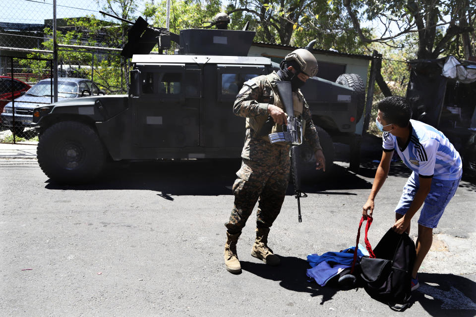 A soldier checks a man´s backpack at the exit of the Las Palmas Community, a neighborhood that is supposed to be under the control of the Barrio 18 Gang in San Salvador, El Salvador, Sunday, March 27, 2022. El Salvador's congress has granted President Nayib Bukele request to declare a state of emergency, amid a wave of gang-related killings over the weekend. (AP Photo/Salvador Melendez)