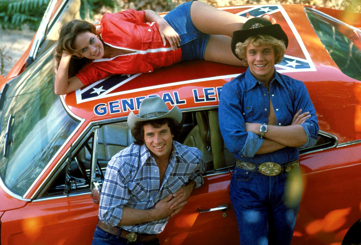 From left to right: Catherine Bach, Tom Wopat and John Schneider pose alongside the General Lee featured in 'The Dukes of Hazzard' (CBS / Courtesy: Everett Collection)