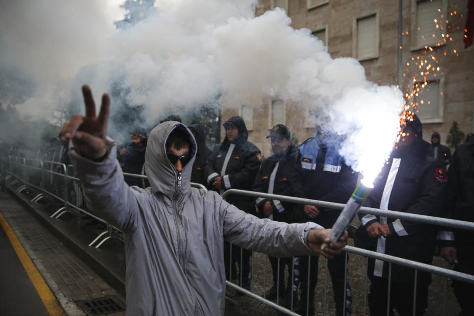 A protester gestures as he holds a flare in front of a police formation during an anti-government rally in Tirana, Albania, Saturday, April 13, 2019. Albanian opposition parties have gathered supporters calling for the government's resignation and an early parliamentary election. (AP Photo/Visar Kryeziu)