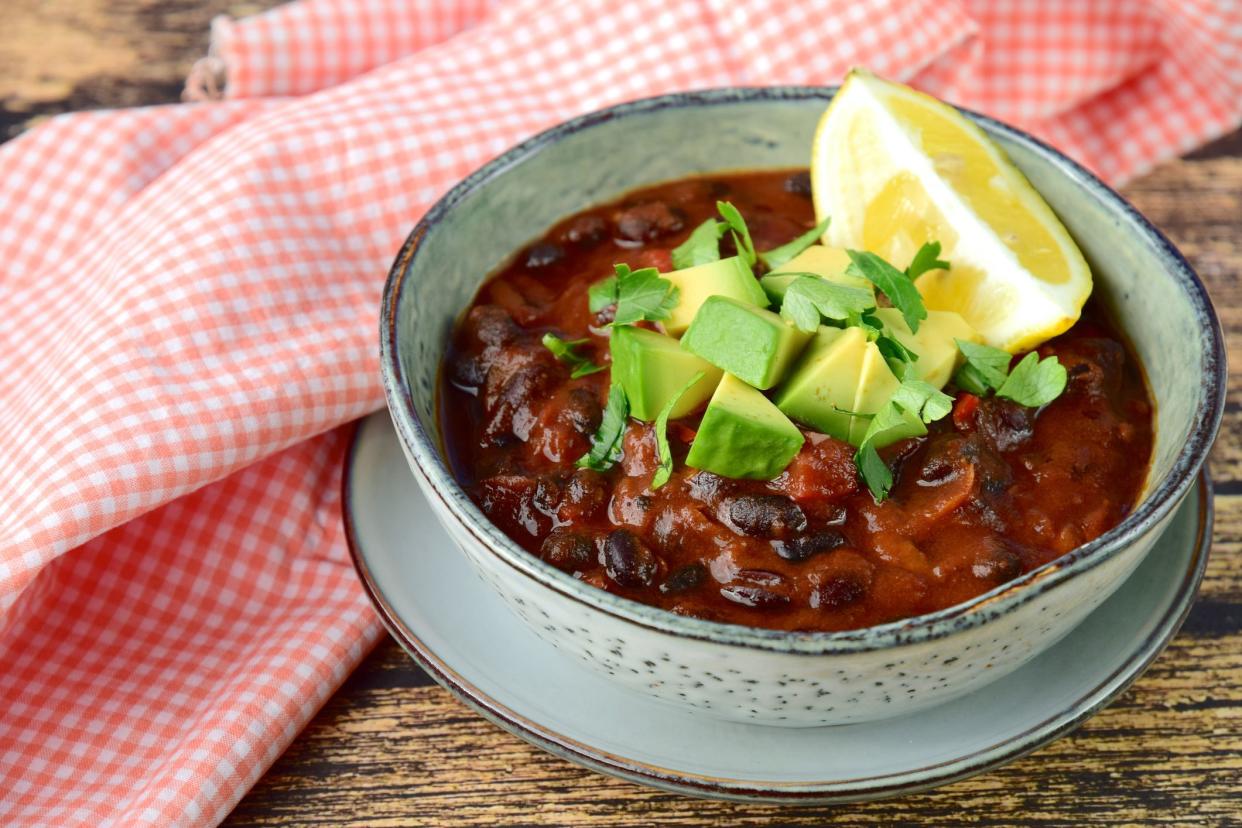 Homemade vegan black bean chili tomato soup with diced avocado and chopped parsley served with lemon