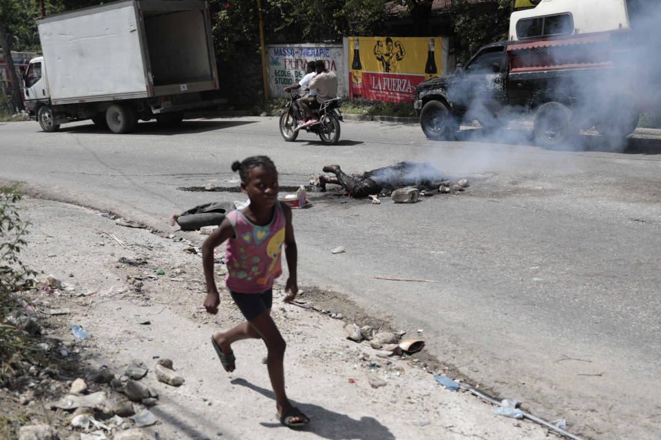 FILE - A child runs past the body of a man accused of stealing a motorcycle who was killed and then set on fire, in the Petion-ville neighborhood of Port-au-Prince, Haiti, July 16, 2023. After more than nine months of unsuccessful appeals from the U.N. for a country to lead an effort to restore order in Haiti, on July 29th Kenya’s foreign minister said that his government is considering leading a force and to deploy police 1000 police officers. (AP Photo/Odelyn Joseph, File)