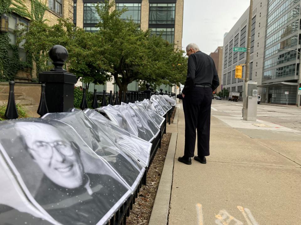 The Rev. James Connell, a retired priest in the Milwaukee archdiocese, looks at photos of abusive priests outside the Cathedral of St. John the Evangelist in Milwaukee on Monday. Advocates tied the photos to a fence outside the cathedral to protest the funeral of former Archbishop Rembert Weakland, which is set for Tuesday at the cathedral.