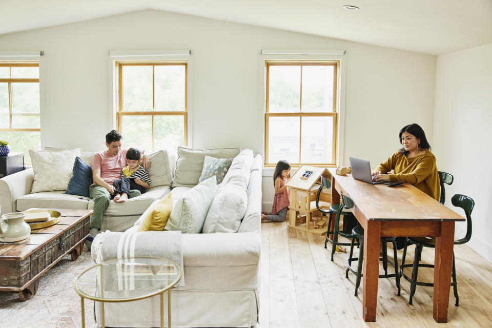 Wide shot of mother working on laptop while family plays in living room