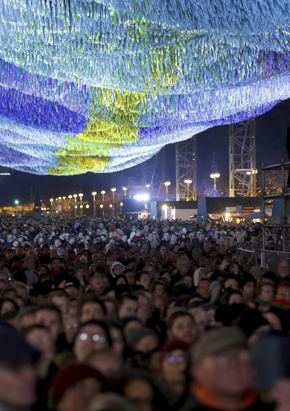 Visitors stay underneath the skynet artwork 'Visions In Motion' in front of the Brandenburg Gate as they attend stage presentations to celebrate the 30th anniversary of the fall of the Berlin Wall in Berlin, Germany, Saturday, Nov. 9, 2019. (AP Photo/Michael Sohn)