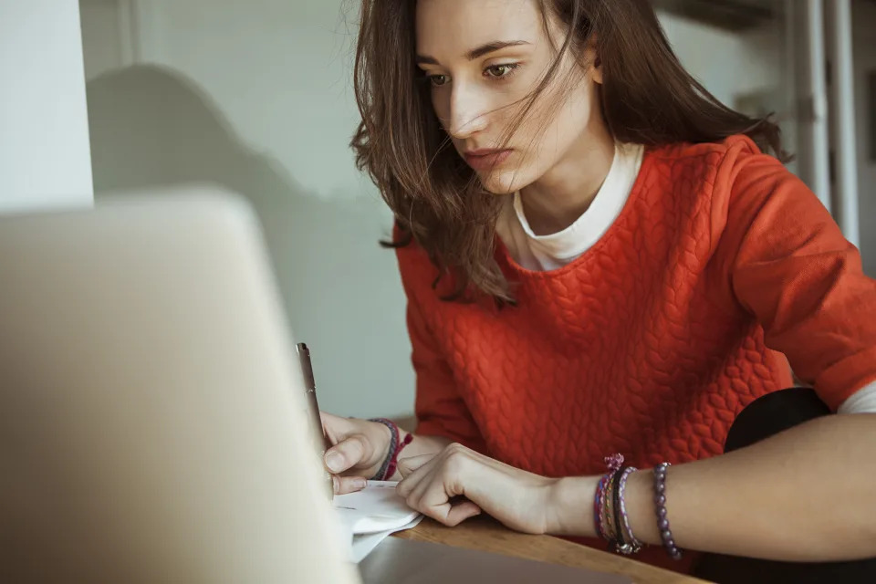 Young pistillate   utilizing laptop and taking notes