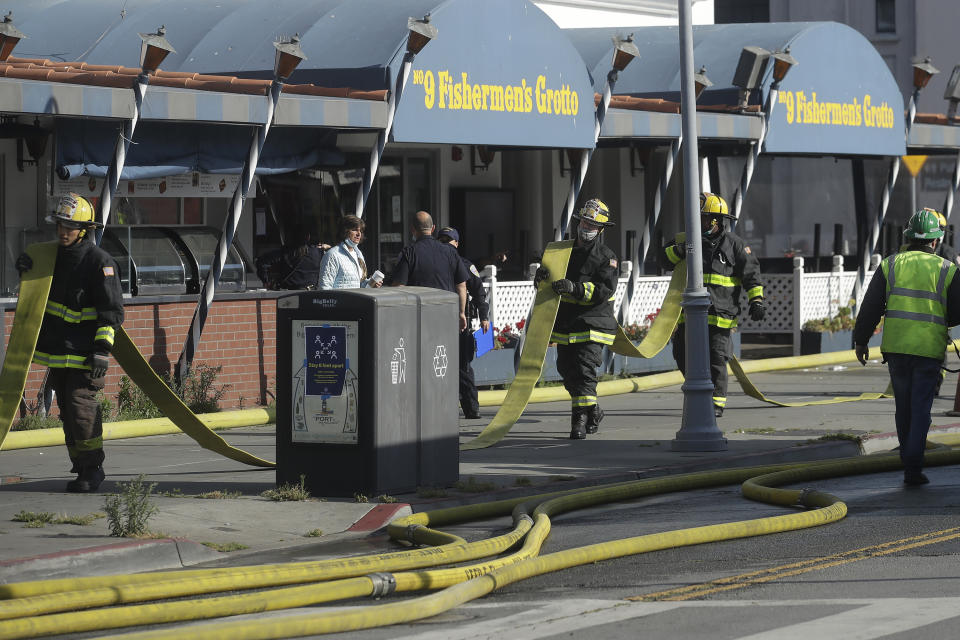 Fire officials carry a hose in front of The Grotto restaurant after a fire broke out before dawn at Fisherman's Wharf in San Francisco, Saturday, May 23, 2020. A warehouse was destroyed. Fire officials said no injuries have been reported Saturday morning and firefighters are making multiple searches to ensure no one was inside the building on Pier 45. (AP Photo/Jeff Chiu)