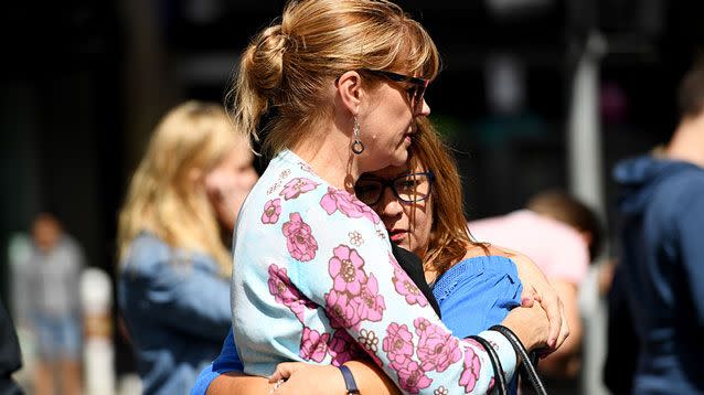 Mourners embrace where flowers are being laid on the corner of Bourke and Elizabeth Streets. Source: AAP