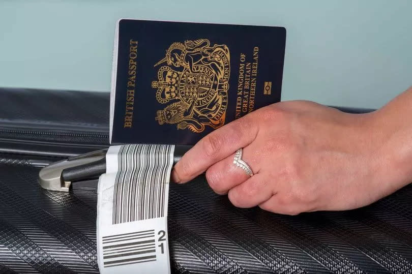 A new dark blue colored British passport held in a travellers hand with holiday suitcase.