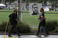 People walk past an image of George Floyd on a fence around Cal Anderson Park, Thursday, June 11, 2020, inside what is being called the "Capitol Hill Autonomous Zone" in Seattle. Following days of violent confrontations with protesters, police in Seattle have largely withdrawn from the neighborhood, and protesters have created a festival-like scene that has President Donald Trump fuming. (AP Photo/Ted S. Warren)