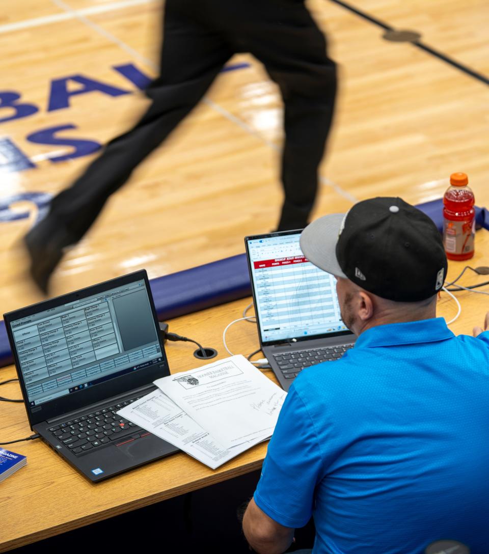 An official runs past dual computers used by Aaron Pitman on Tuesday, Jan. 9, 2024, at a Ben Davis vs. Brebeuf boy’s basketball game. While client organizations can opt for live announcing, Pitman and colleague Jake Hinson can announce games entirely virtually, even from off-site.