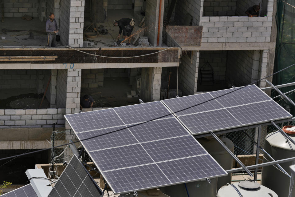 Construction workers work next to solar panels installed on a building in Beirut, Lebanon, Thursday, May 30, 2024. Lebanese caretaker Minister of Economy and Trade Amin Salam said Lebanon's political class as well as fuel companies and private electricity providers in Lebanon blocked an offer by gas-rich Qatar to build three renewable energy power plants to ease the crisis-hit nation's decades-old electricity crisis. (AP Photo/Bilal Hussein)