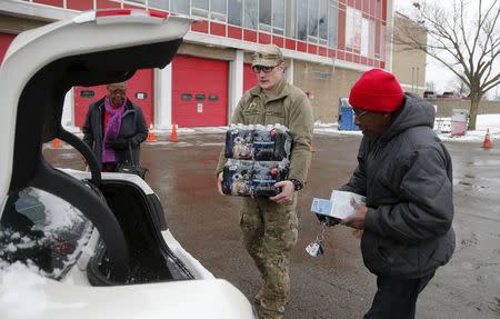 Michigan National Guard Staff Sergeant William Phillips assists two Flint residents with bottled water and a water filter at a fire station in Flint, Michigan January 13, 2016. REUTERS/Rebecca Cook