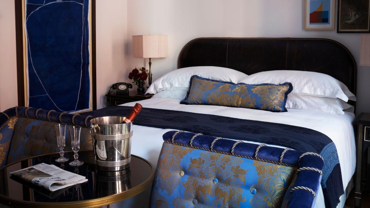  A shot of a double bed in a room in the hotel NoMad London.  Sparkling wine sits in an ice bucket on a side table in the forground, and in the background is one of NoMad's signature double beds 