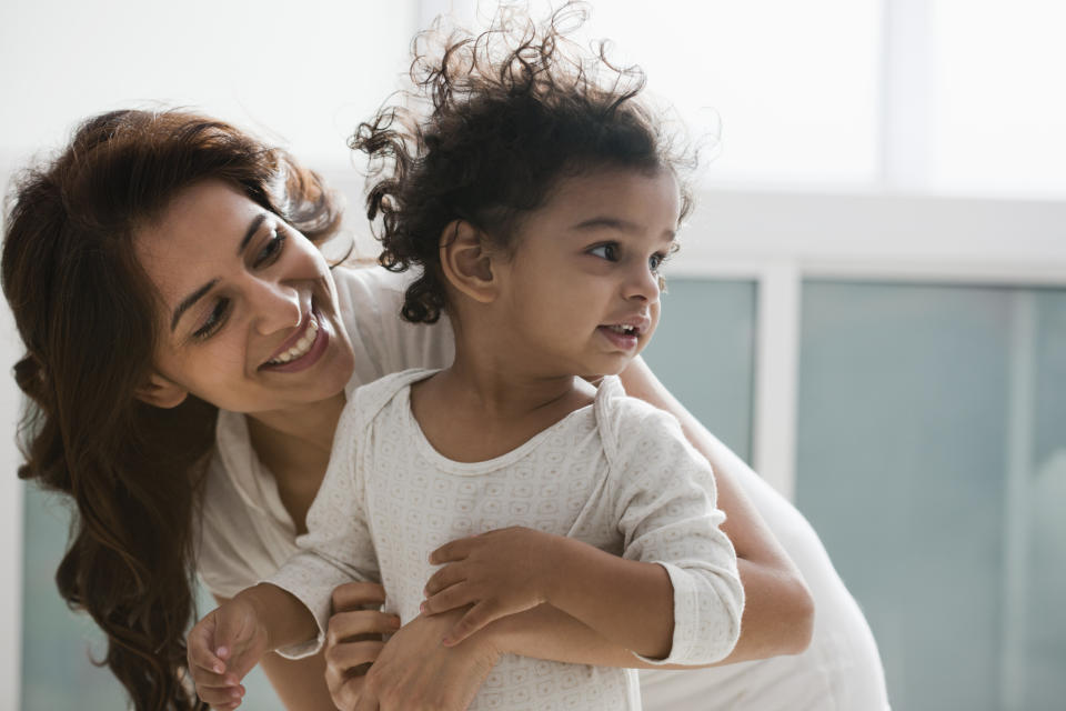 Mom smiling at child in her arms, both casually dressed, in a well-lit room