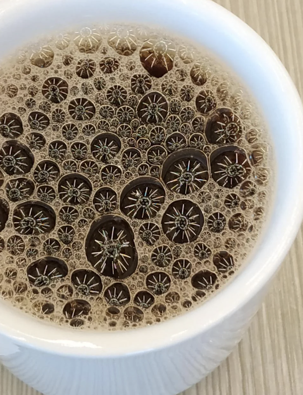 A close-up view of a cup filled with bubbly coffee, showcasing the intricate patterns formed by the bubbles