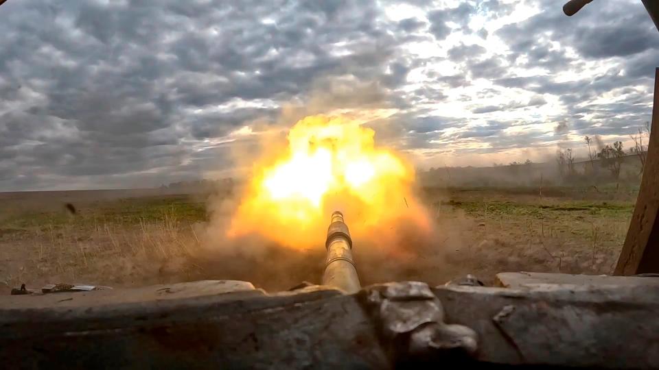 Fire erupts from the barrel of a T-90 tank on a scarred battlefield in Ukraine.