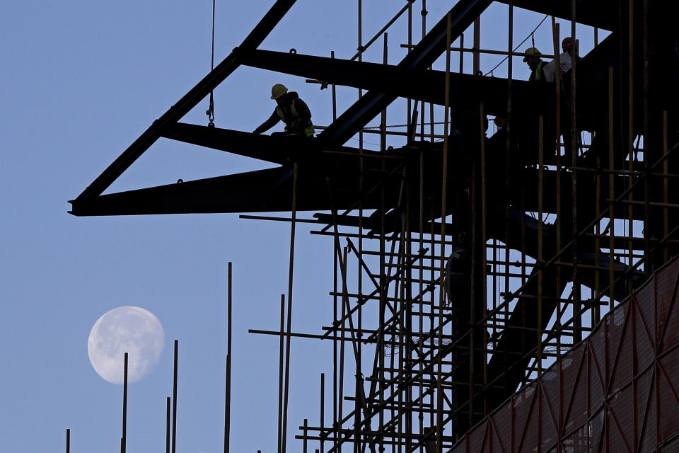 In this Tuesday, Dec. 25, 2018, file photo, workers load cables on a steel frames at a shopping mall under renovation, with a backdrop of the moon, in Beijing, Tuesday, Dec. 25, 2018. (AP Photo/Andy Wong, File)