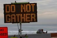 A woman stretches near a warning sign on the beach as new stay-at-home orders begin in Southern California